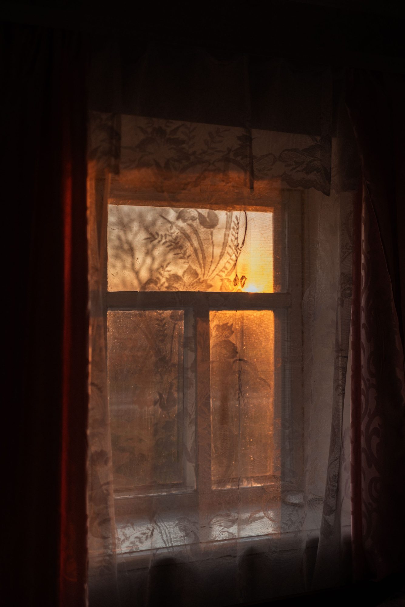 A still evening at home, warm light glowing through a lace-curtained window