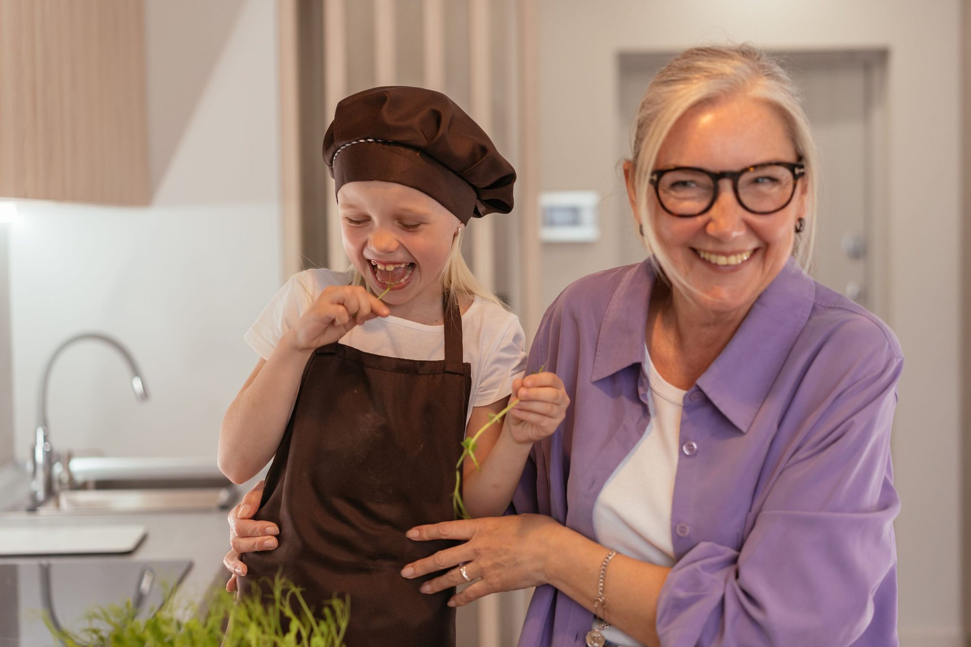 A grandmother and granddaughter laughing together while cooking in the kitchen