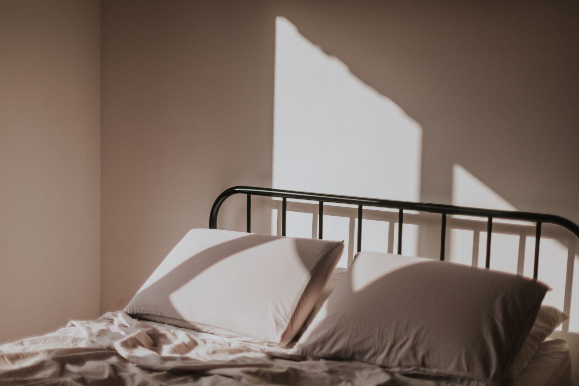 A still bedroom in soft early-morning light, the bed made and the night over