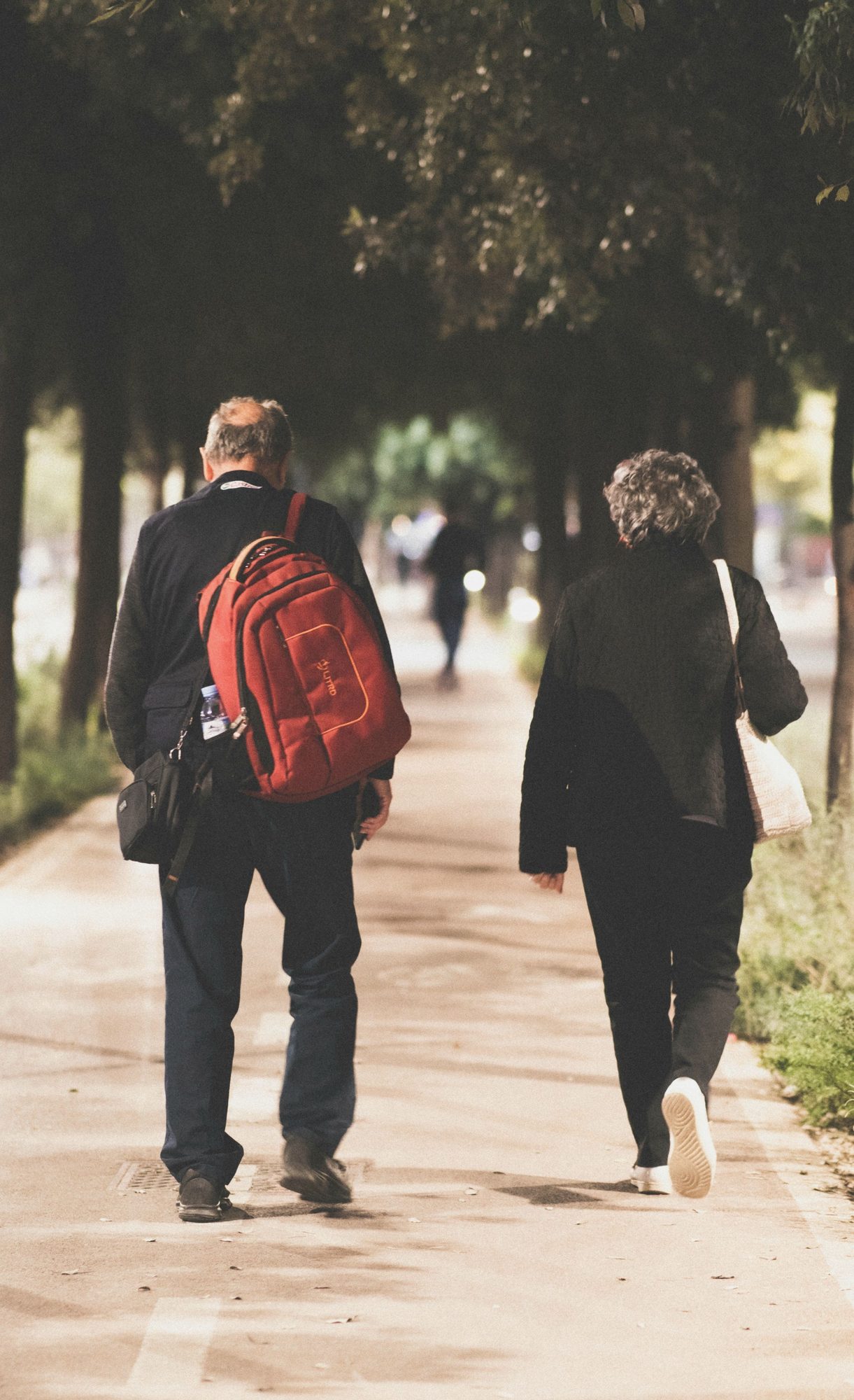 An older couple heading out for a walk together along a tree-lined path